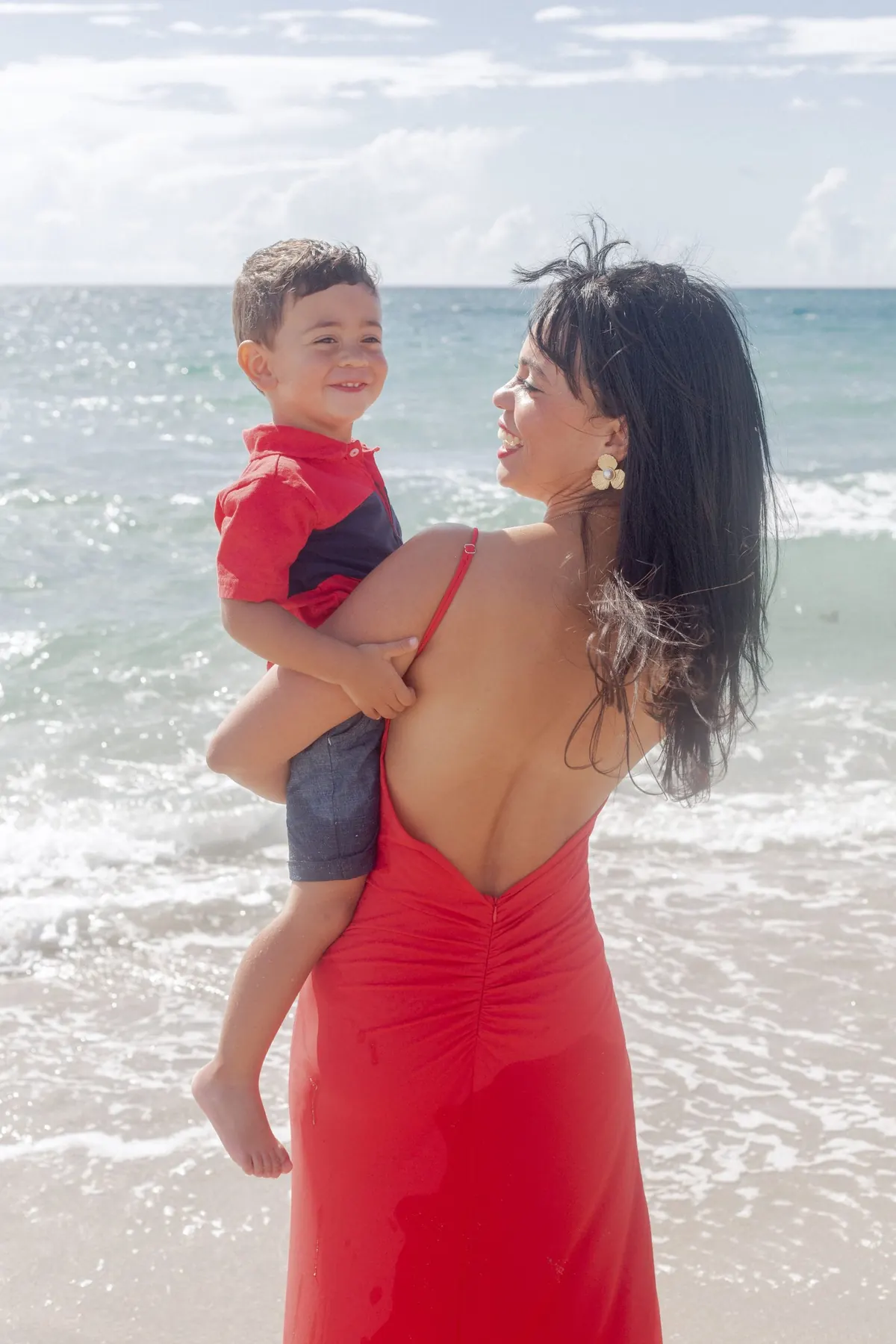 Mom in a red dress holding her son at the shoreline